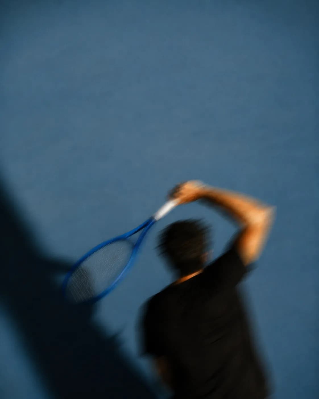 A tennis player mid-serve on a blue court, caught in motion blur.