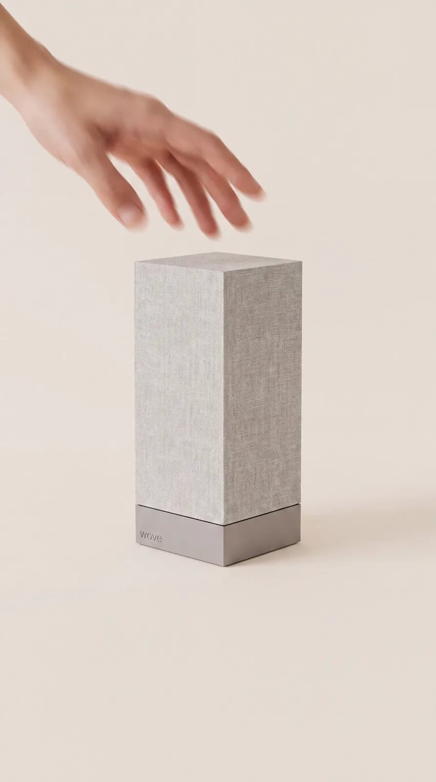 A hand reaching toward the wove device, a small linen-wrapped tower on a warm cream surface.
