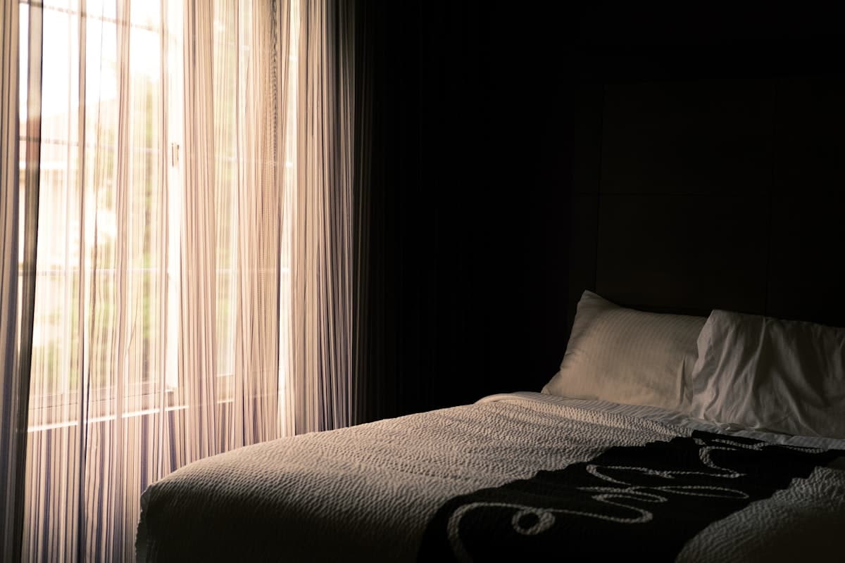 Warm golden light spilling through a striped curtain onto an unmade bed.