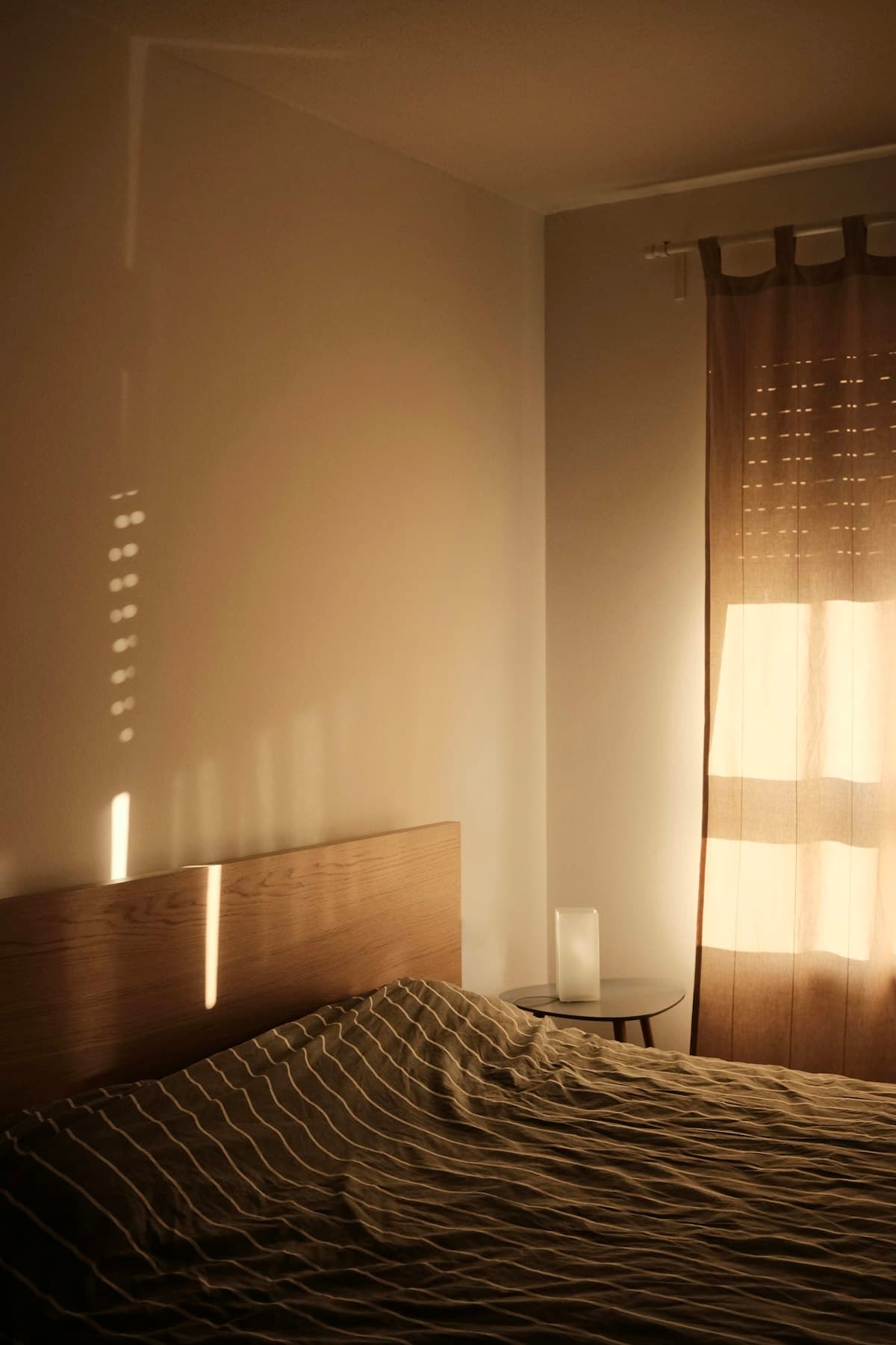 Golden-hour light across striped bed linen beside a glowing curtain.