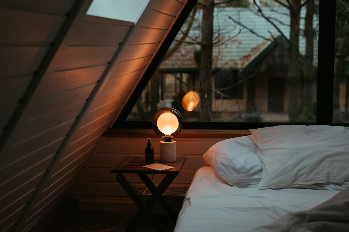 A round bulb lamp glowing on a nightstand beside a dusk window view.