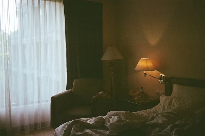 Warm lamplight beside a window with sheer curtains drawn.